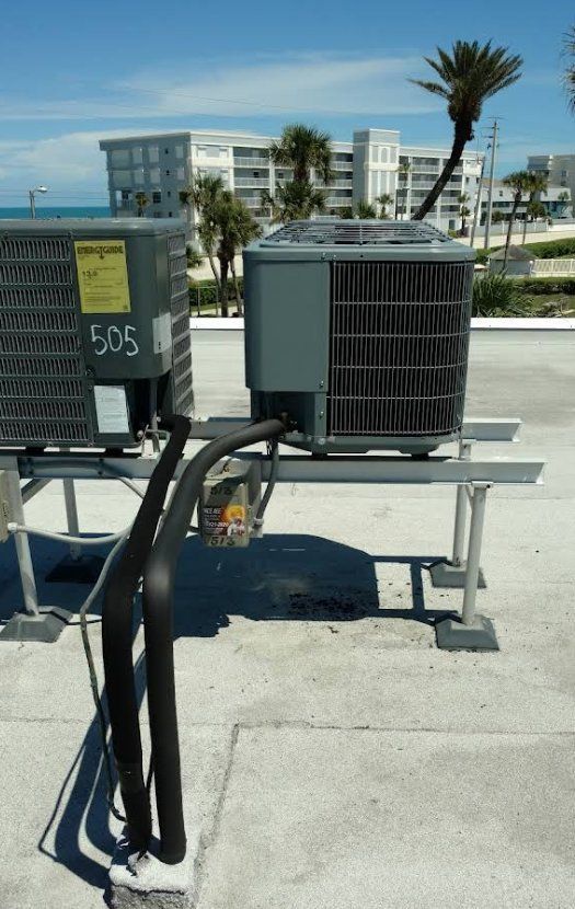 Two air conditioning units on a rooftop with ocean and buildings in the background.