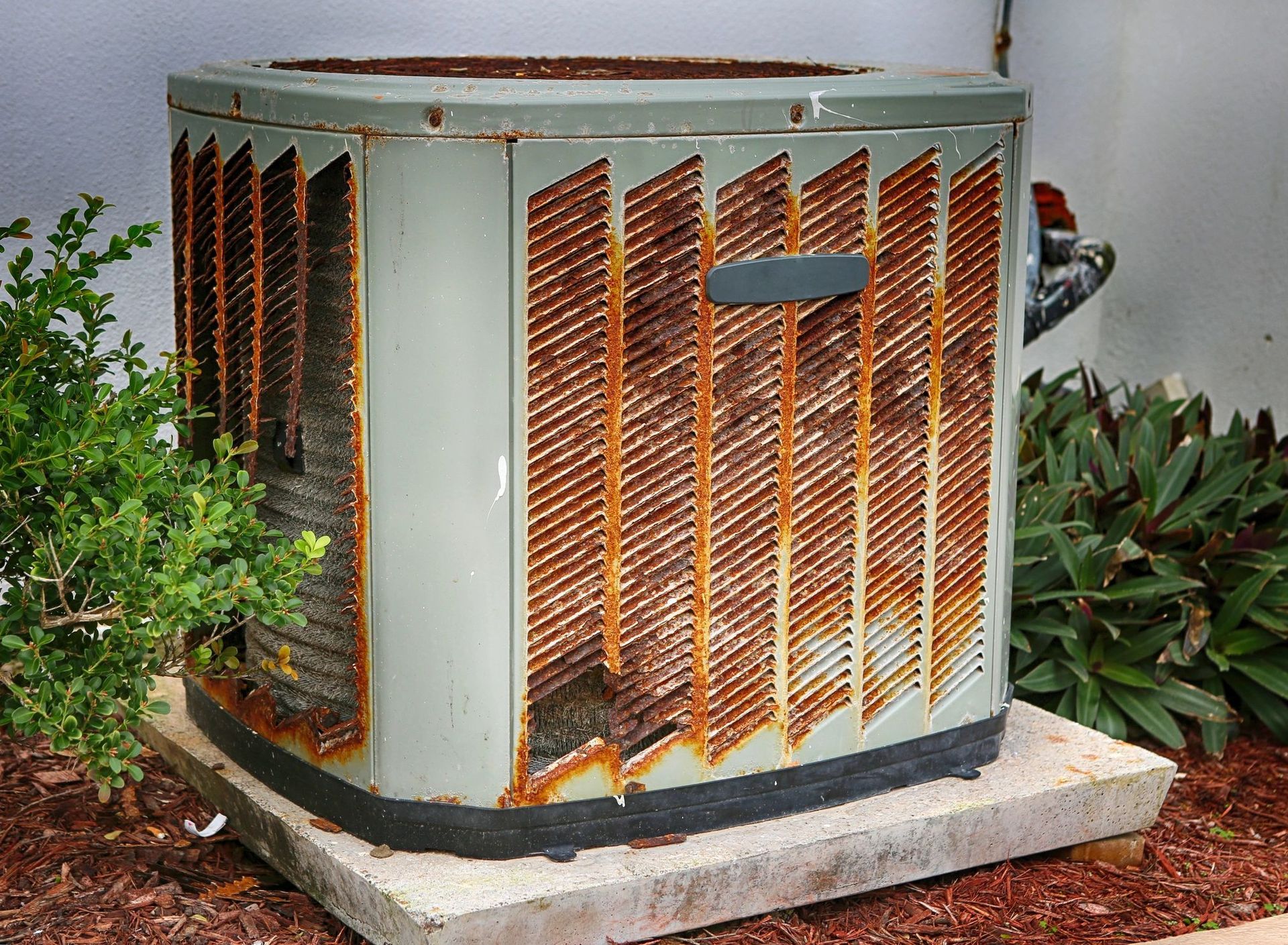 Rusted outdoor air conditioning unit on a concrete base, next to bushes.
