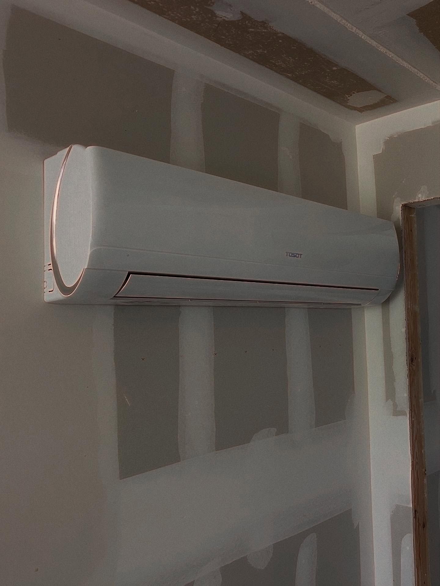 White mini-split air conditioner mounted on a drywall wall in an unfinished room.