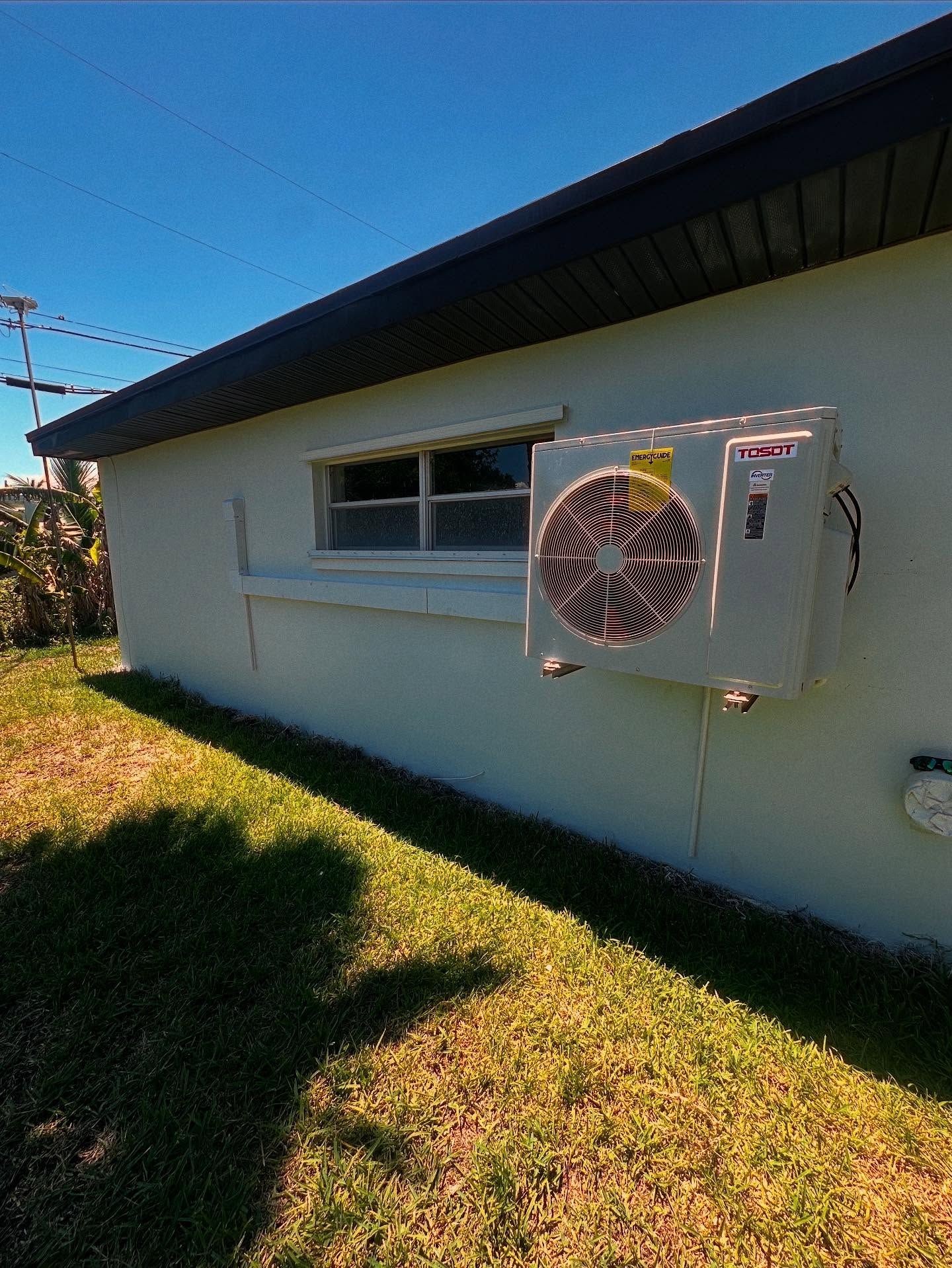 Exterior of a white building with an air conditioning unit attached to the wall, set against a blue sky.