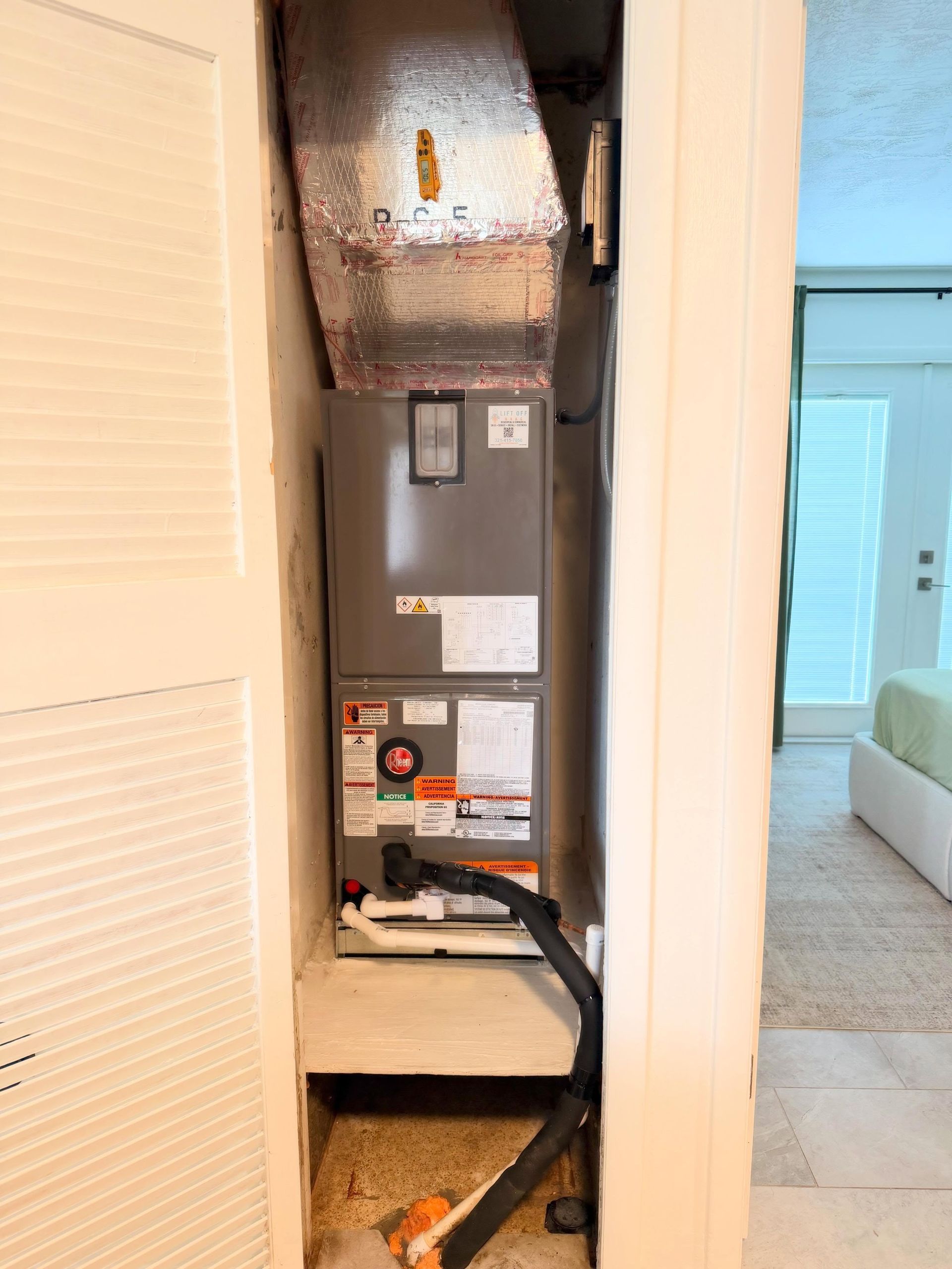 Open HVAC closet with furnace, exposed ducts, and disconnected black hose in a hallway.