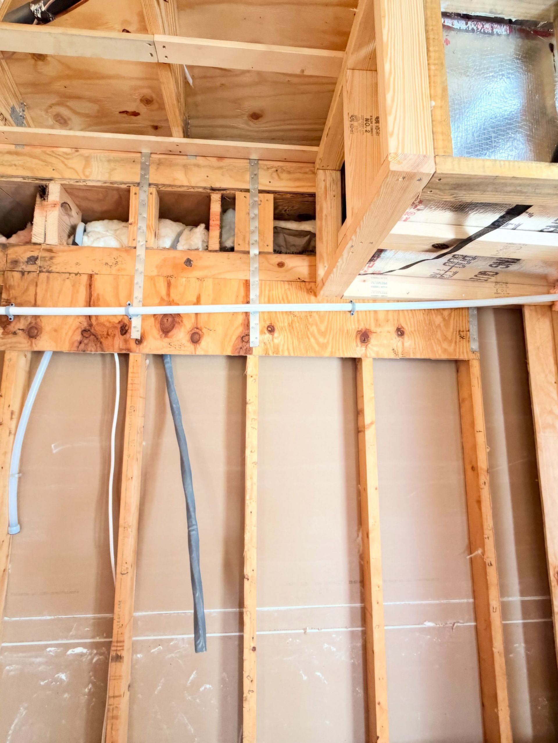 Exposed wall framing and ceiling joists in an unfinished room with electrical wiring and beige insulation.