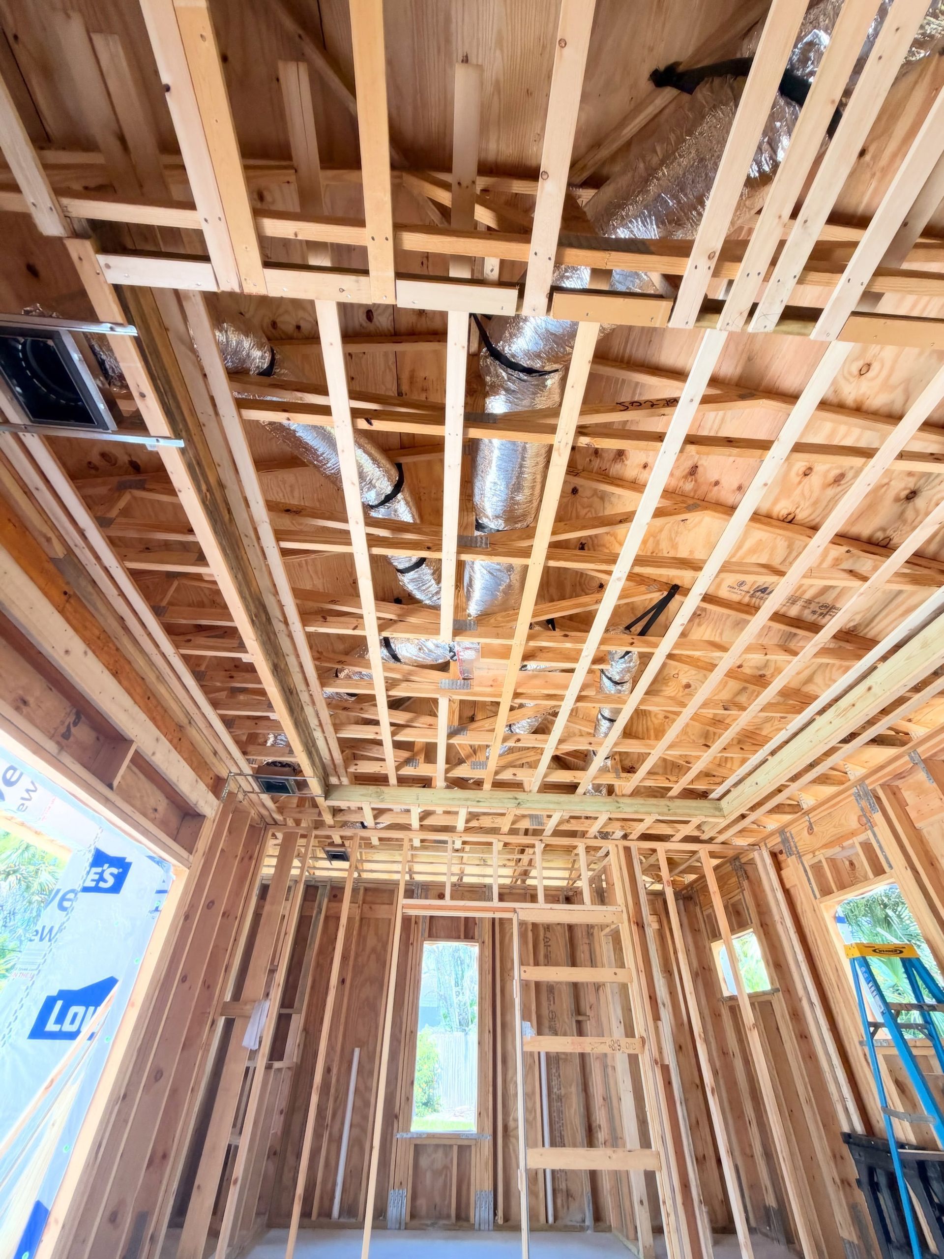 Unfinished house interior with exposed wooden framing, ceiling joists, and ductwork.