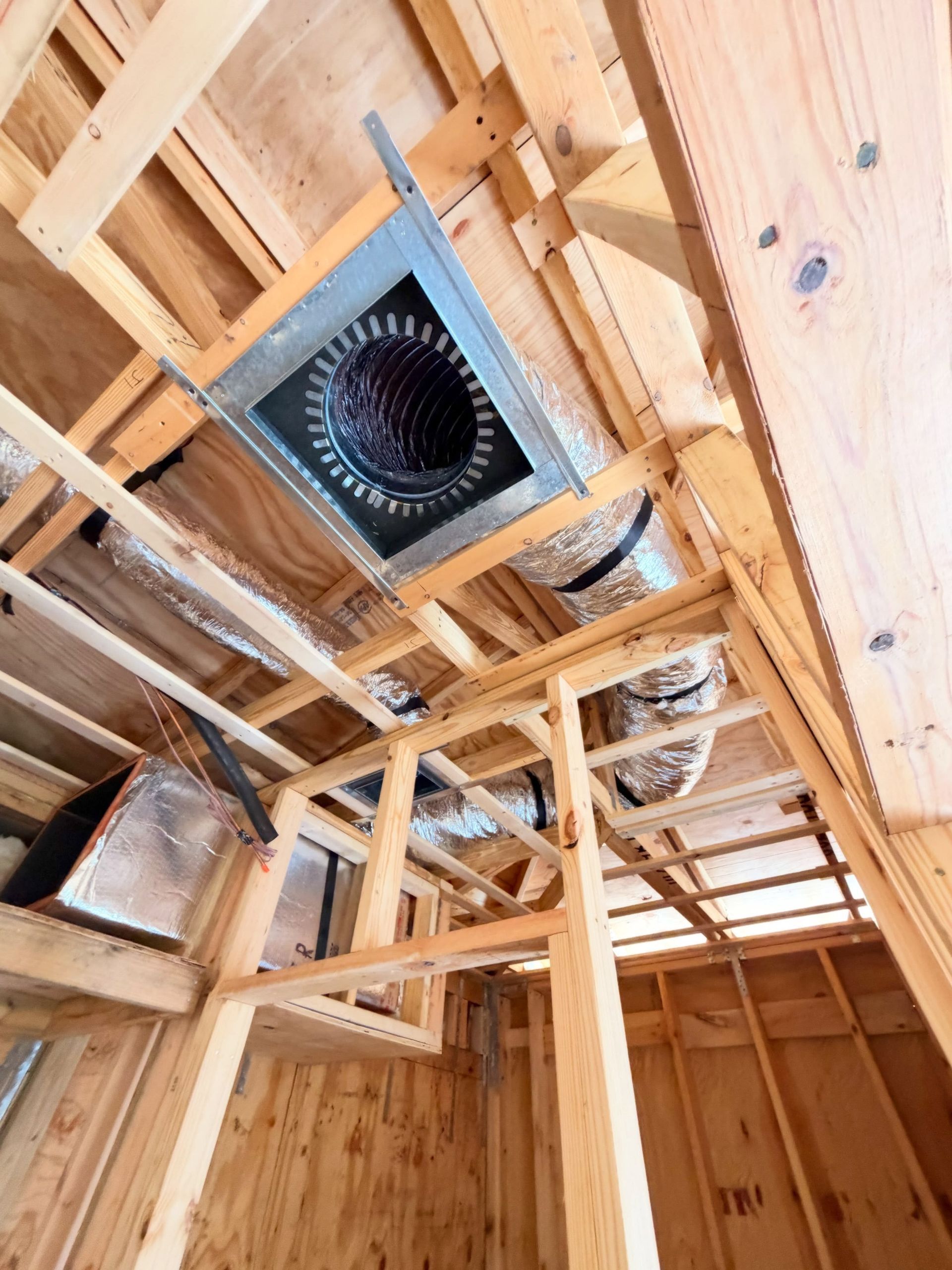 Interior roof framing with exposed wood rafters and a square attic vent fan