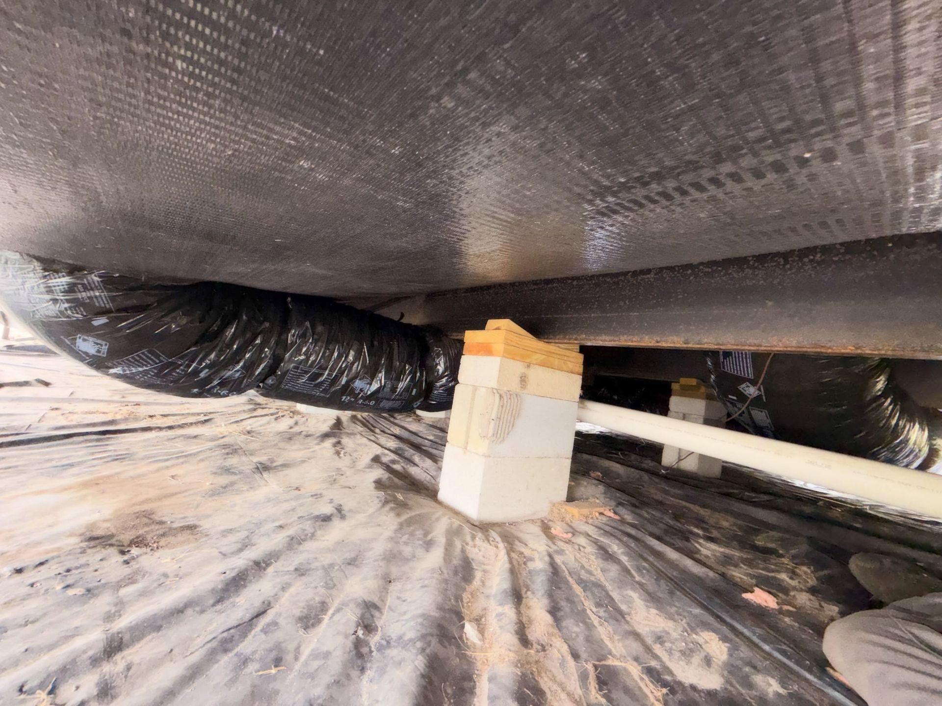 Insulated pipes and ducting under a tarp, with a white container on a dusty floor.