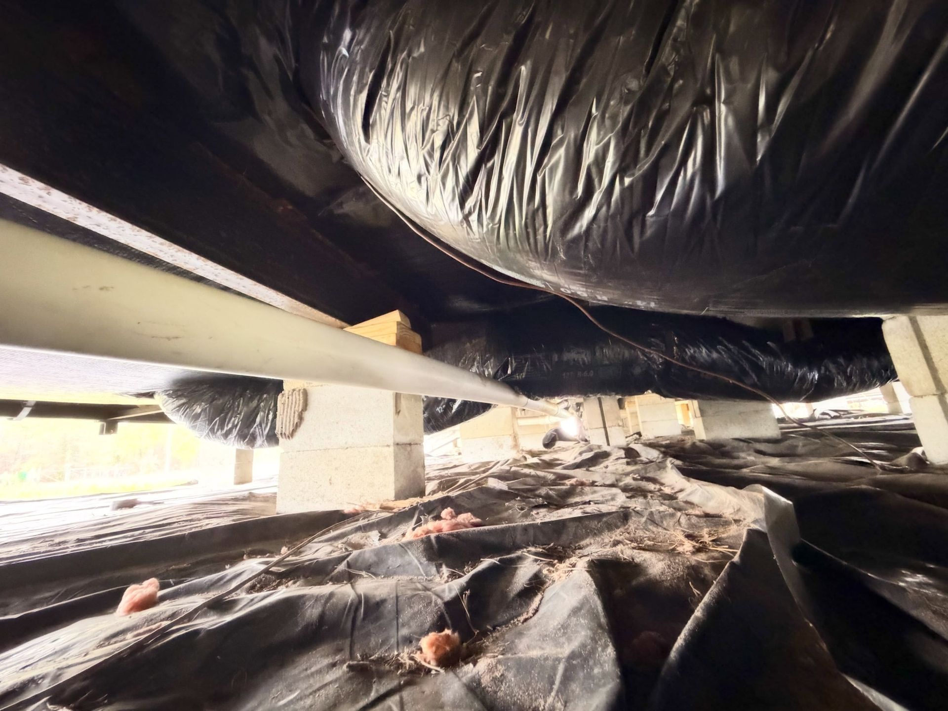 Black plastic-covered insulation under a building, viewed from a low crawlspace angle