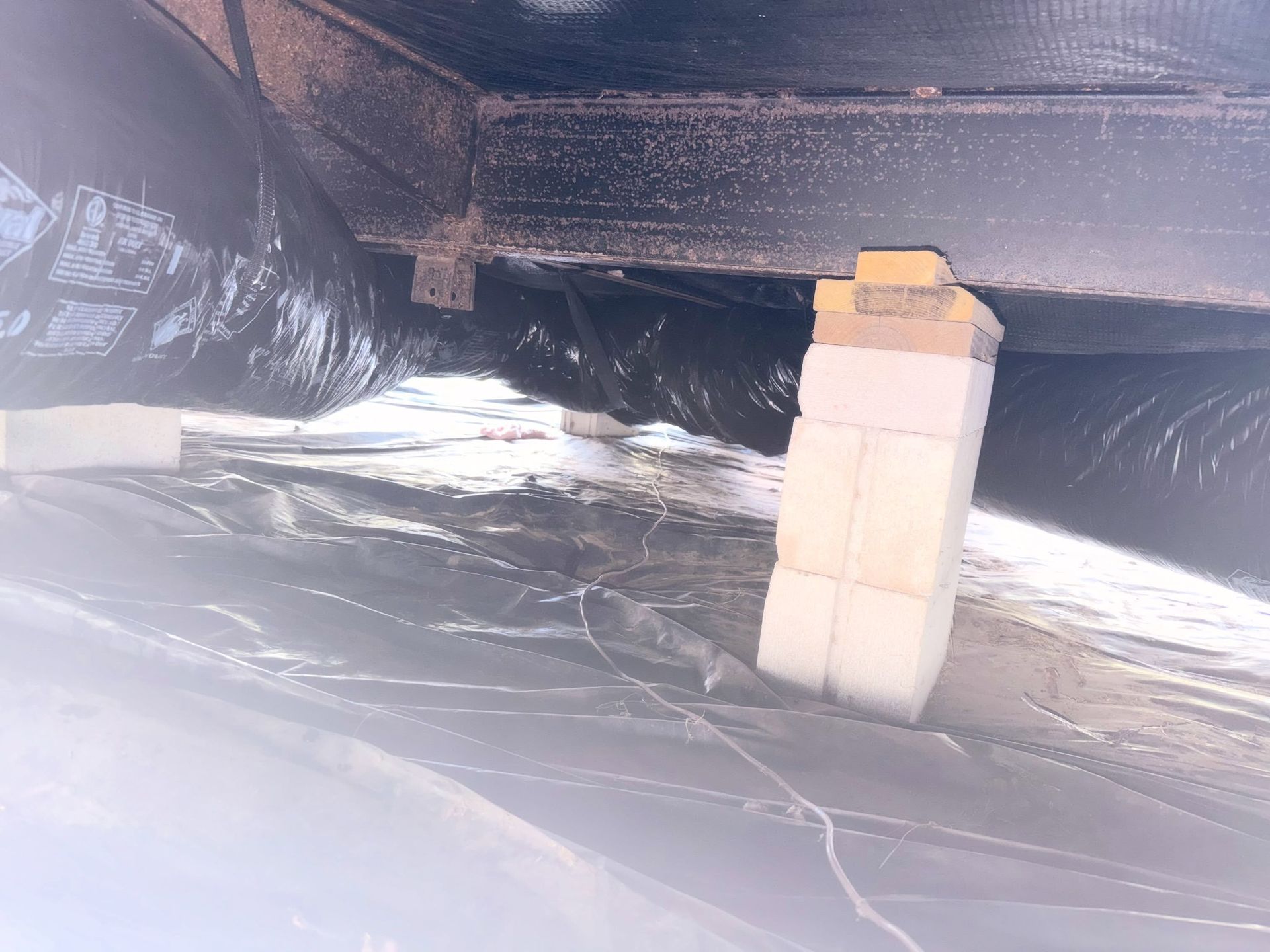 Foil-lined crawlspace with insulation, exposed pipes, and a small white block stack supporting the floor.