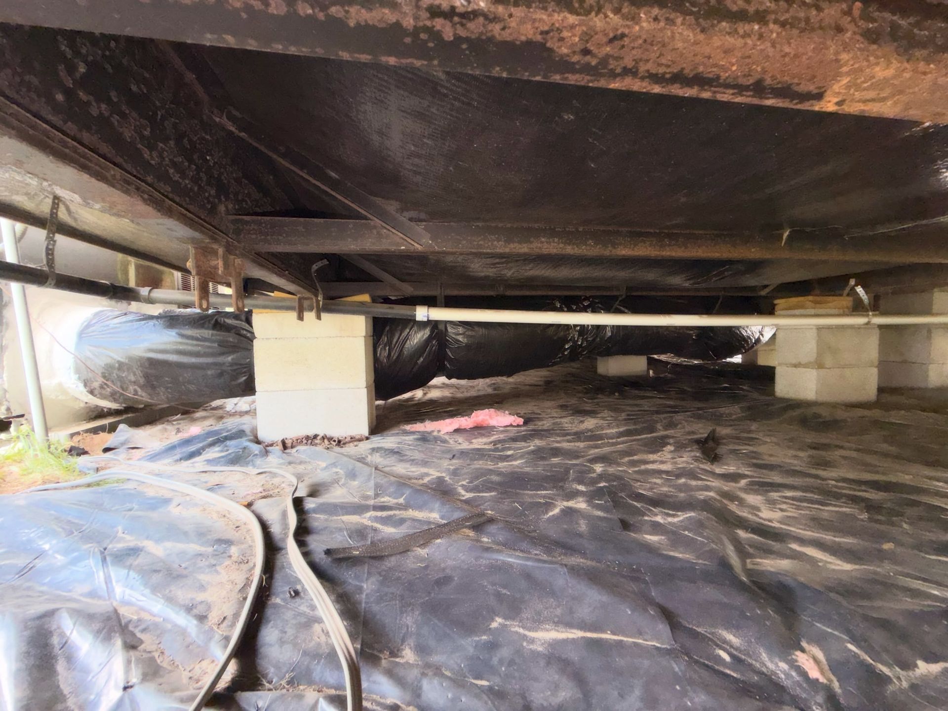 Crawling space under a house, lined with black plastic and supported by concrete piers