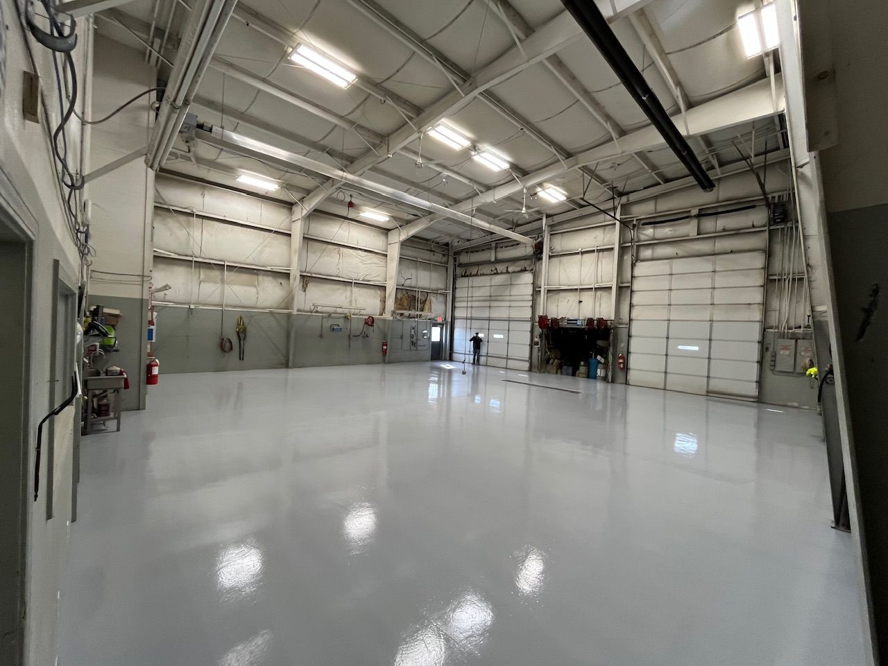 Empty, bright industrial warehouse with shiny, light gray floor. Three garage doors are partially open.