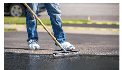 A person is using a broom to spread asphalt on the ground.
