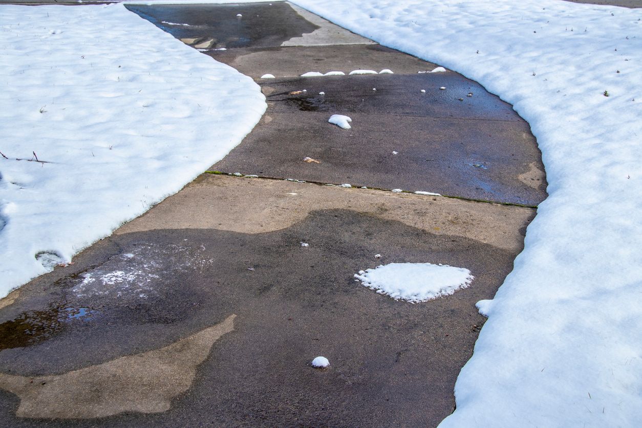 Snowy sidewalk curving through snow-covered ground. Some patches of the sidewalk are wet.