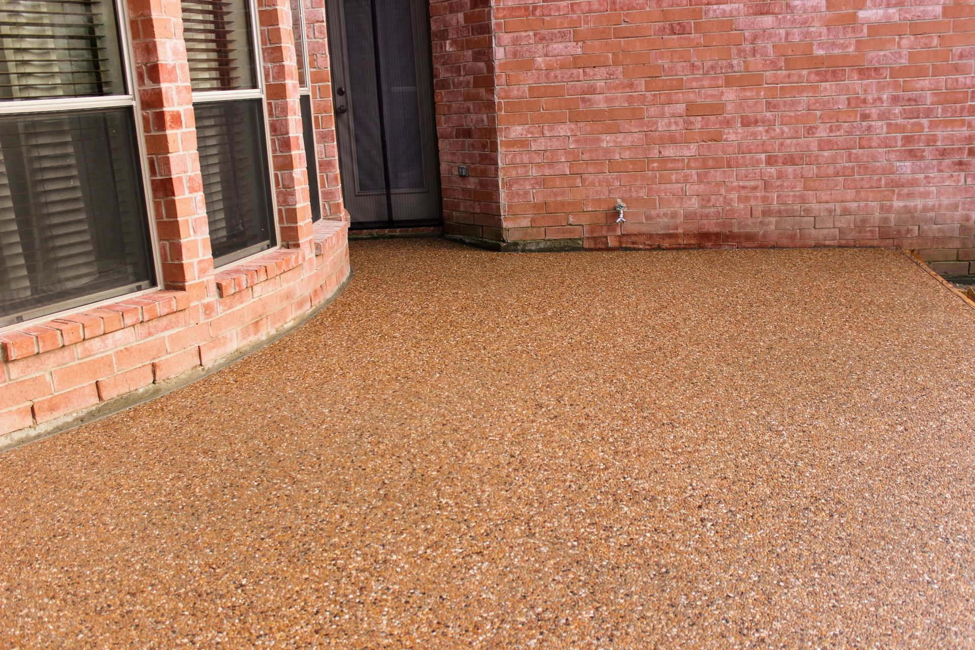 Brown speckled outdoor flooring next to a brick building with a window and door.