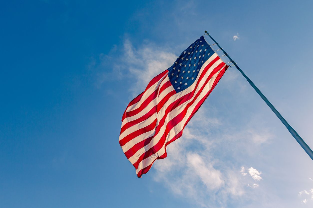 American flag waving against a blue sky with clouds