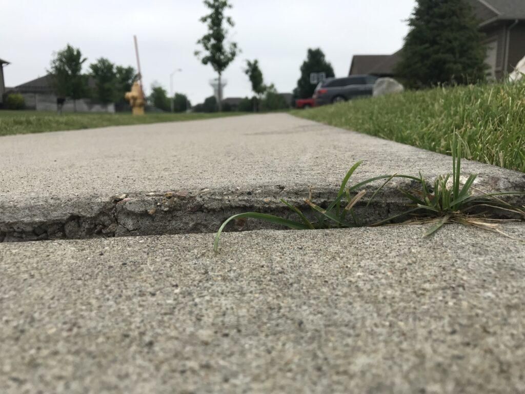 A concrete sidewalk with grass growing out of it