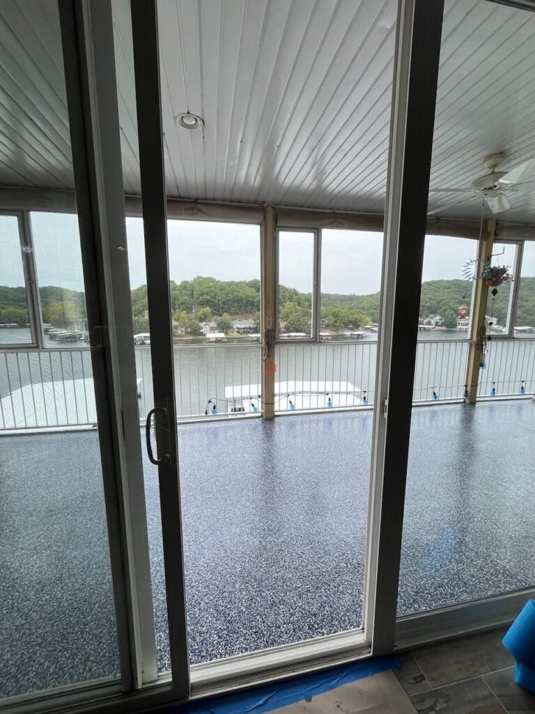Sliding glass doors open to a view of a lake and trees from inside a room with a patterned blue floor and white ceiling.