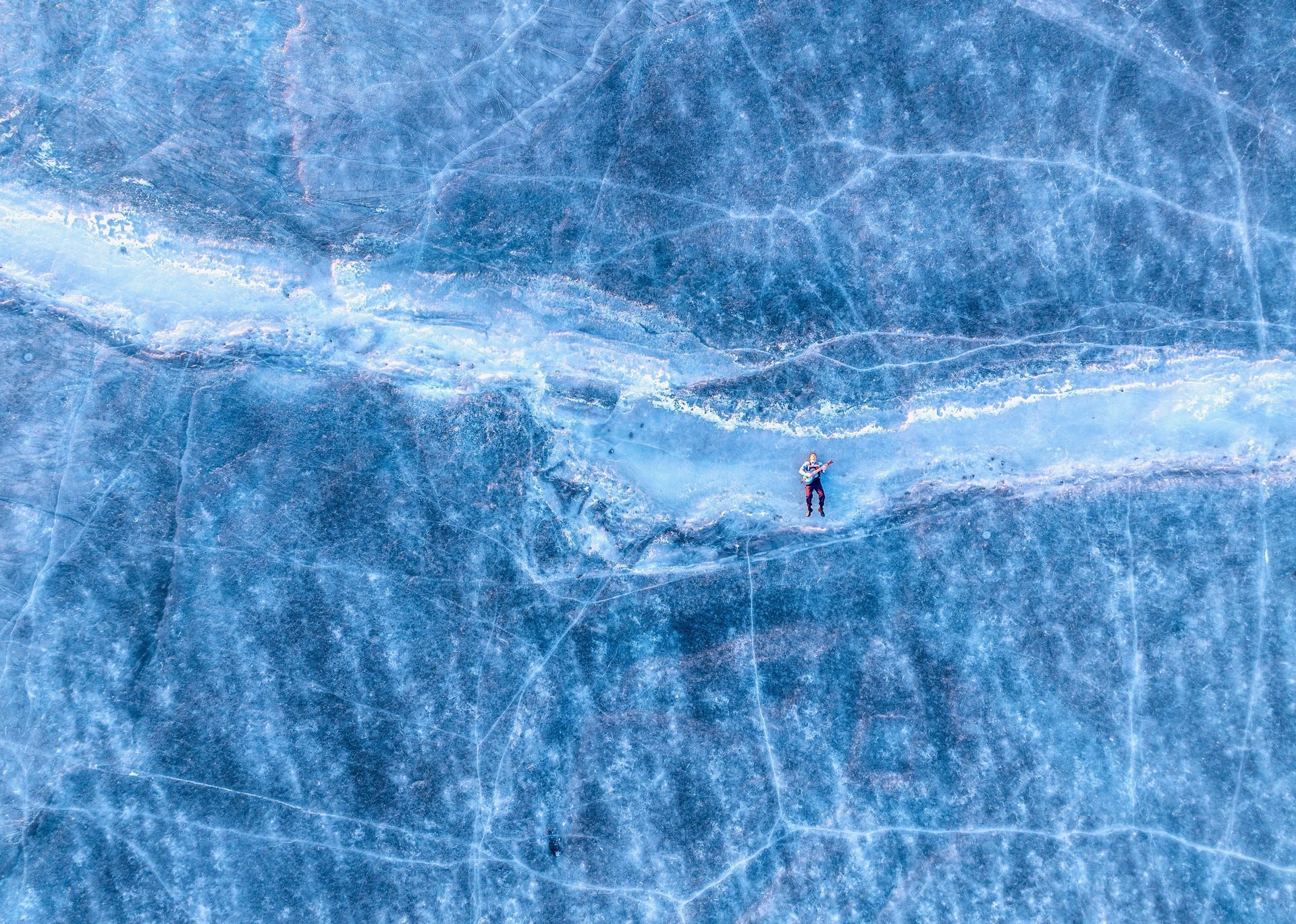 Person lying on cracked, icy blue lake surface.