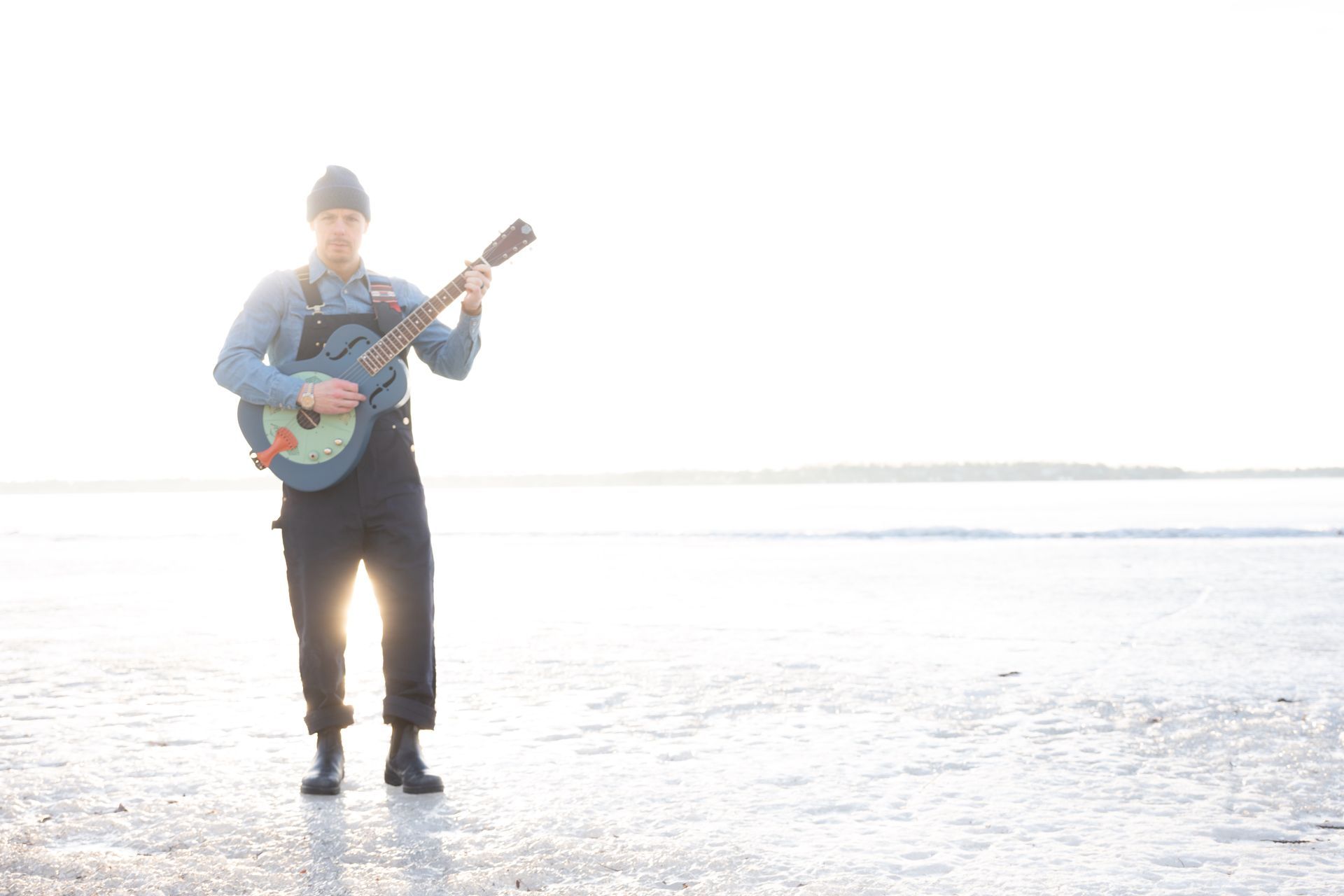 Person playing a banjo on a frozen lake with bright sunlight.