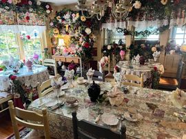 A lavish dining room decorated with roses, floral arrangements, and lace tablecloths, set for a tea party.