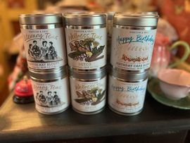 Six silver-lidded tea tins stacked in two rows. Each tin features a different label.