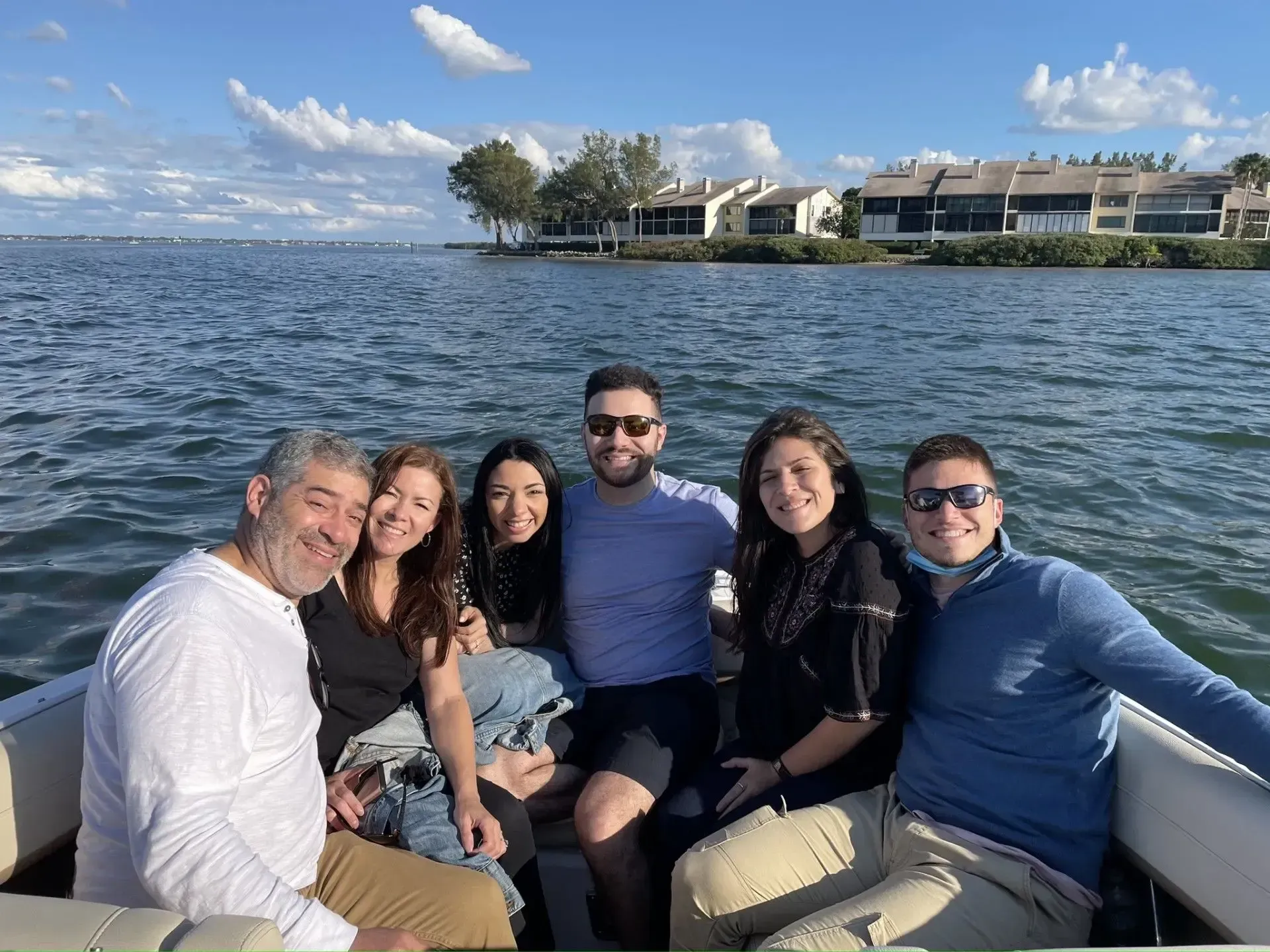 Six friends smiling on a boat with open water and waterfront homes in the background