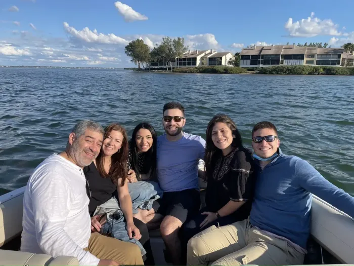 Six friends smiling on a boat with open water and waterfront homes in the background