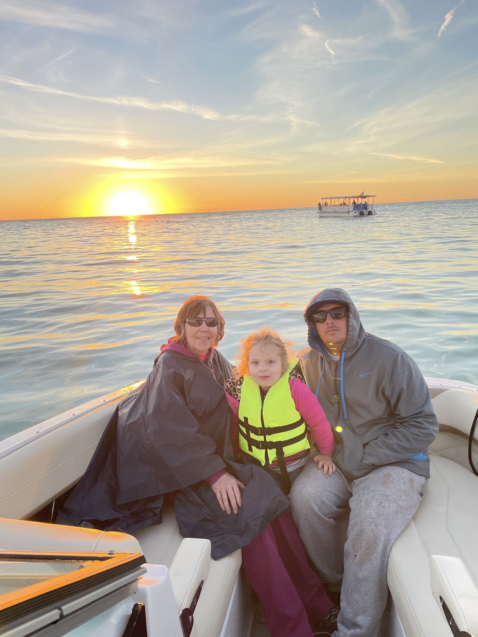 A family is sitting on a boat in the ocean at sunset.