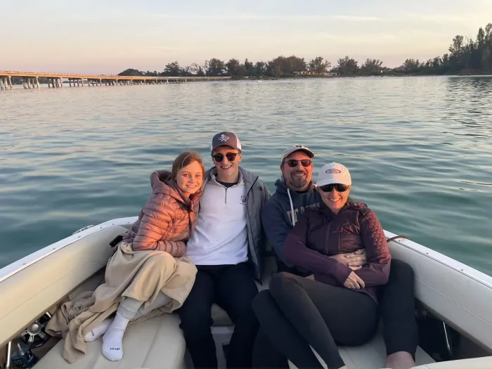 Four people smiling on a boat at sunset, seated close together on calm water.