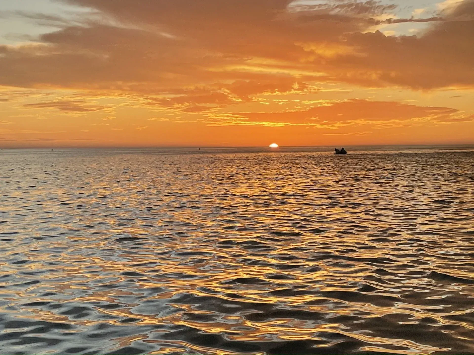 Golden sunset over a calm ocean with rippling water and a small boat near the horizon.