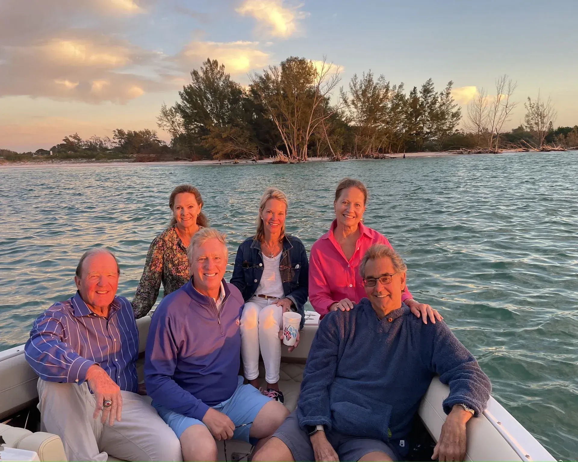 Six people on a boat at sunset on calm water, with a small island in the background.