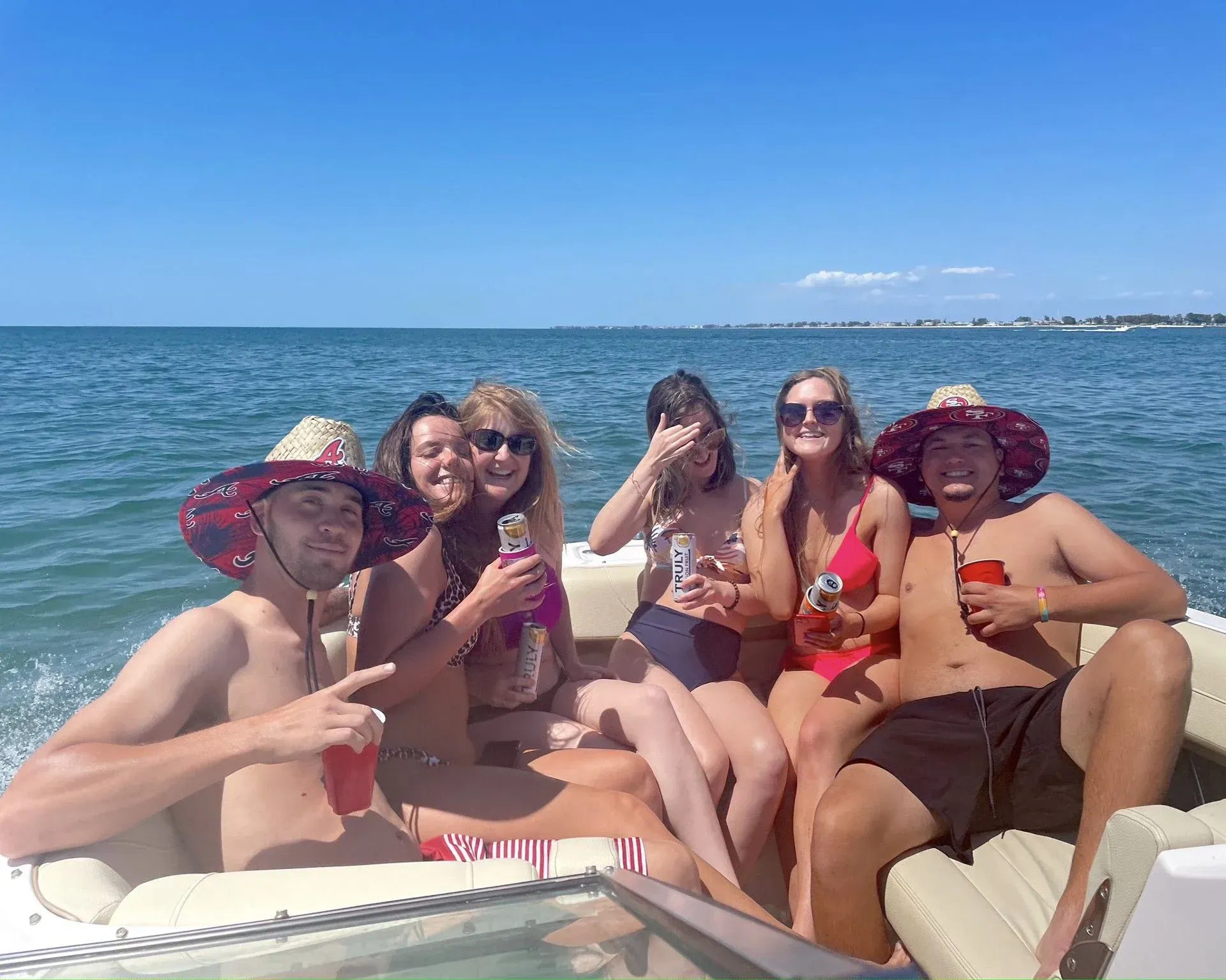 Group lounging on a boat in swimwear, smiling and posing with drinks on a sunny beach.