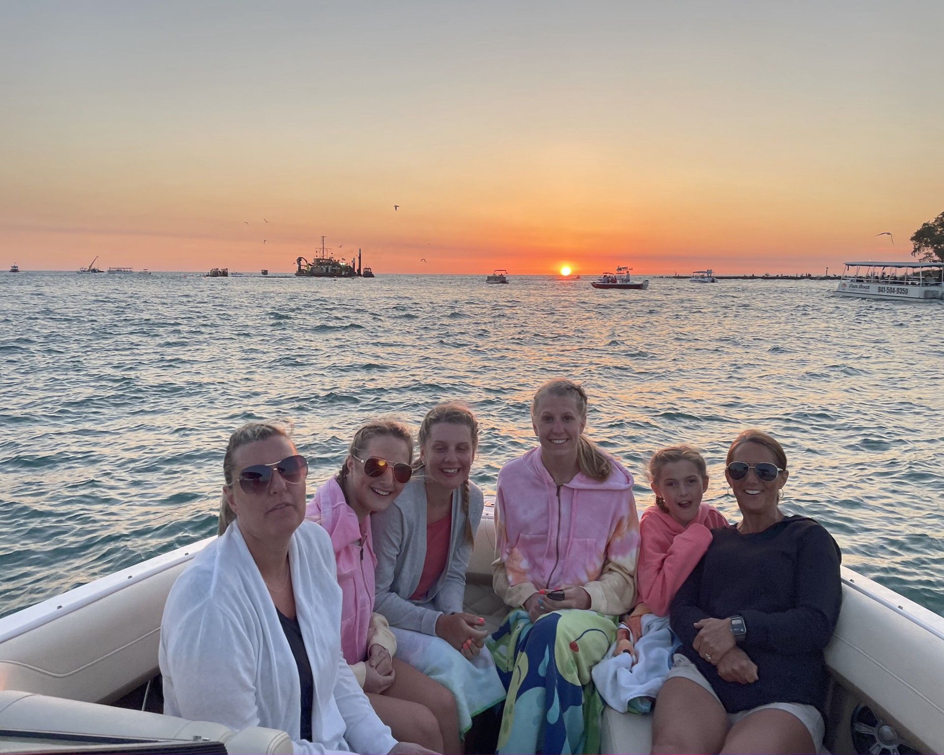 A group of women are sitting on a boat in the ocean at sunset