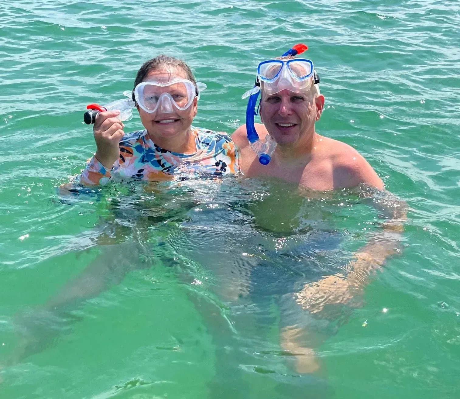 Two snorkelers smiling in green water, wearing masks and snorkels