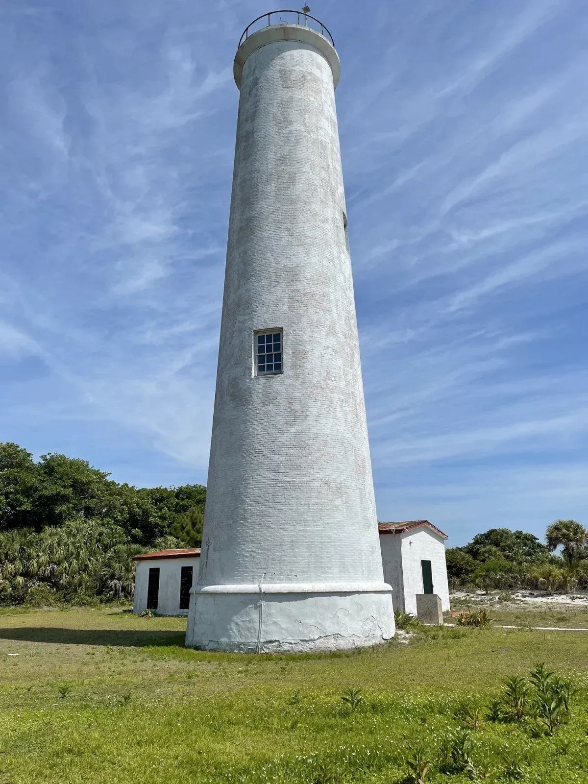 White lighthouse on grassy coast under a blue sky