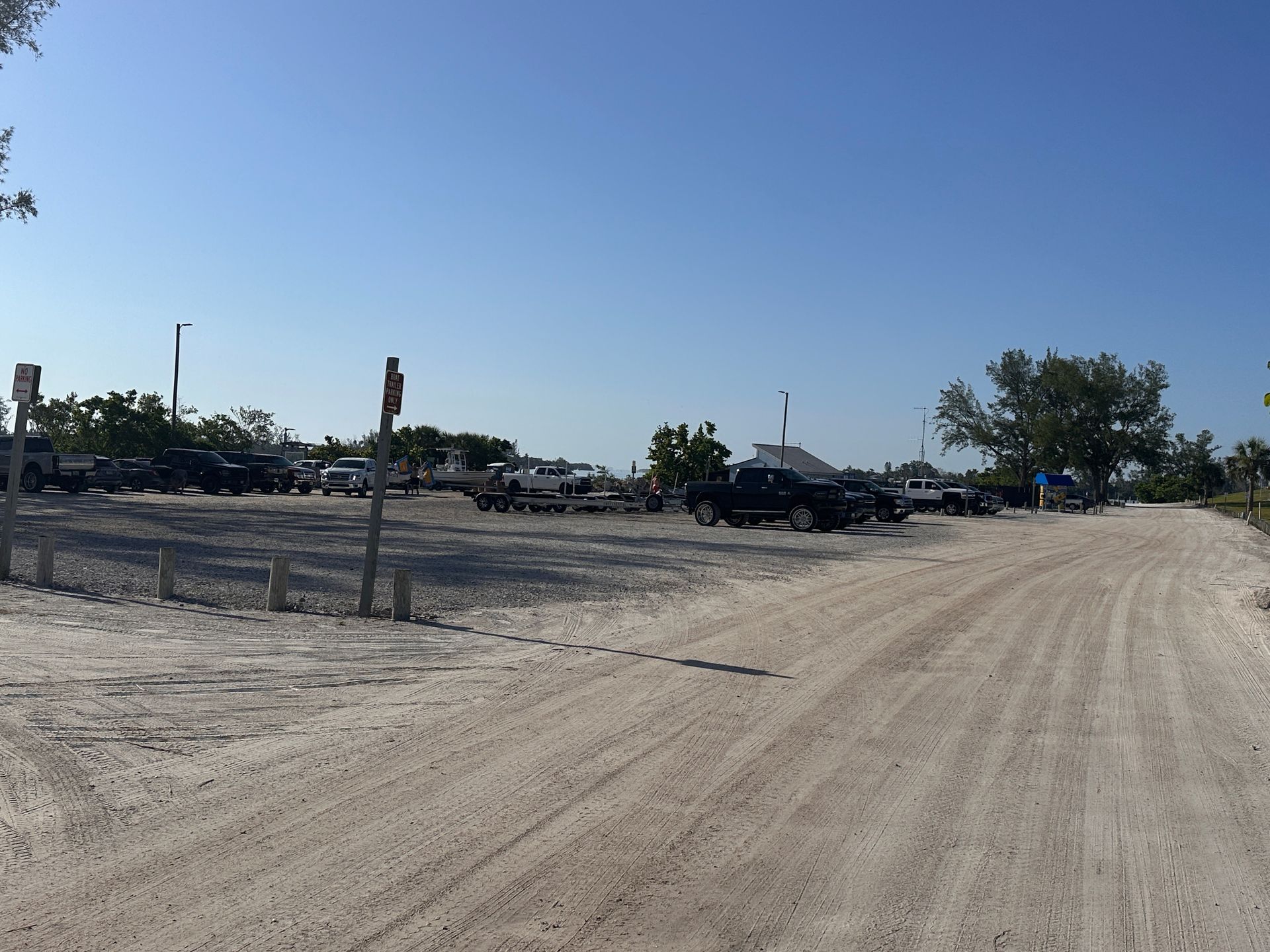 A dirt road lined with parked cars and trucks under a clear sky