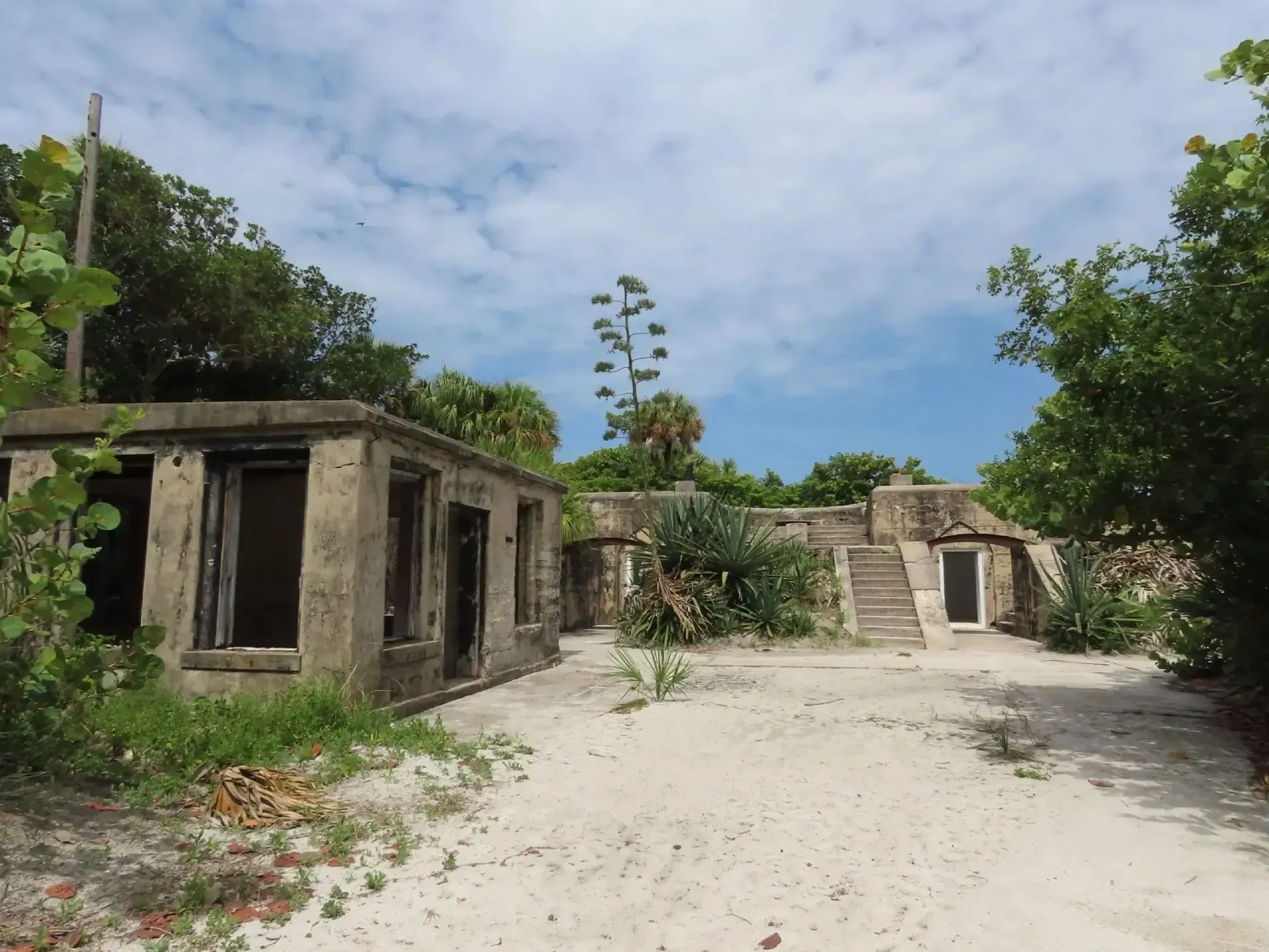 Abandoned concrete buildings in a sandy tropical clearing under a blue sky