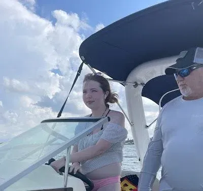Two people riding a boat, steering under a blue canopy on a sunny day