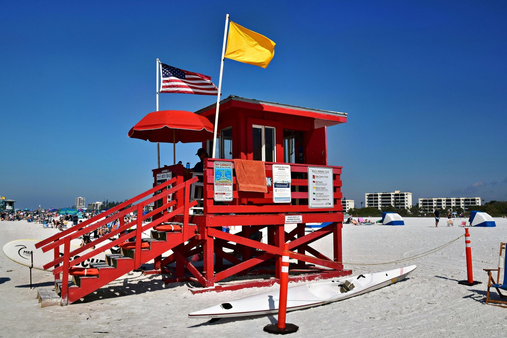 A red lifeguard tower on a beach with a yellow flag