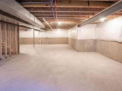 Empty unfinished basement with concrete floor, exposed beams, and insulation on walls.