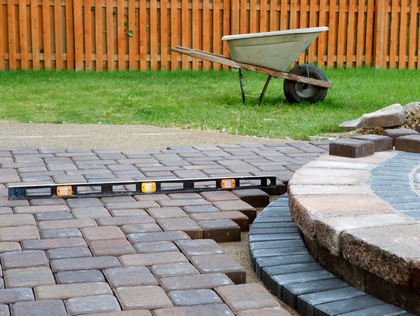 Laying paving stones with a level; wheelbarrow and fence in background.