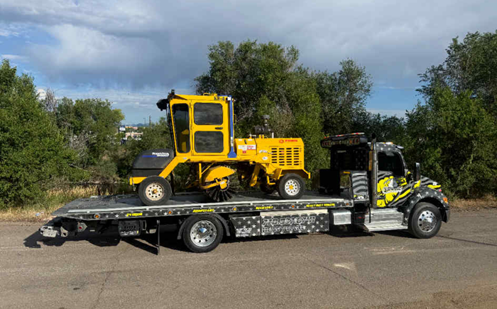 A yellow street sweeper loaded onto a black tow truck.
