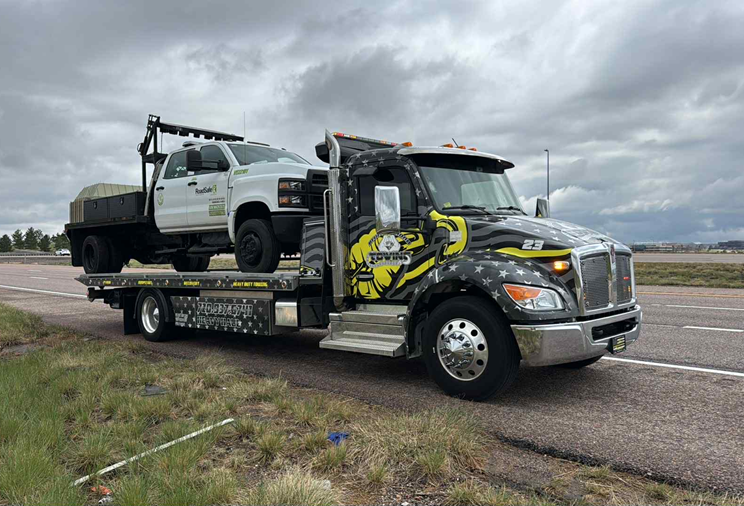 Tow truck hauling a white pickup truck on a highway under cloudy skies.