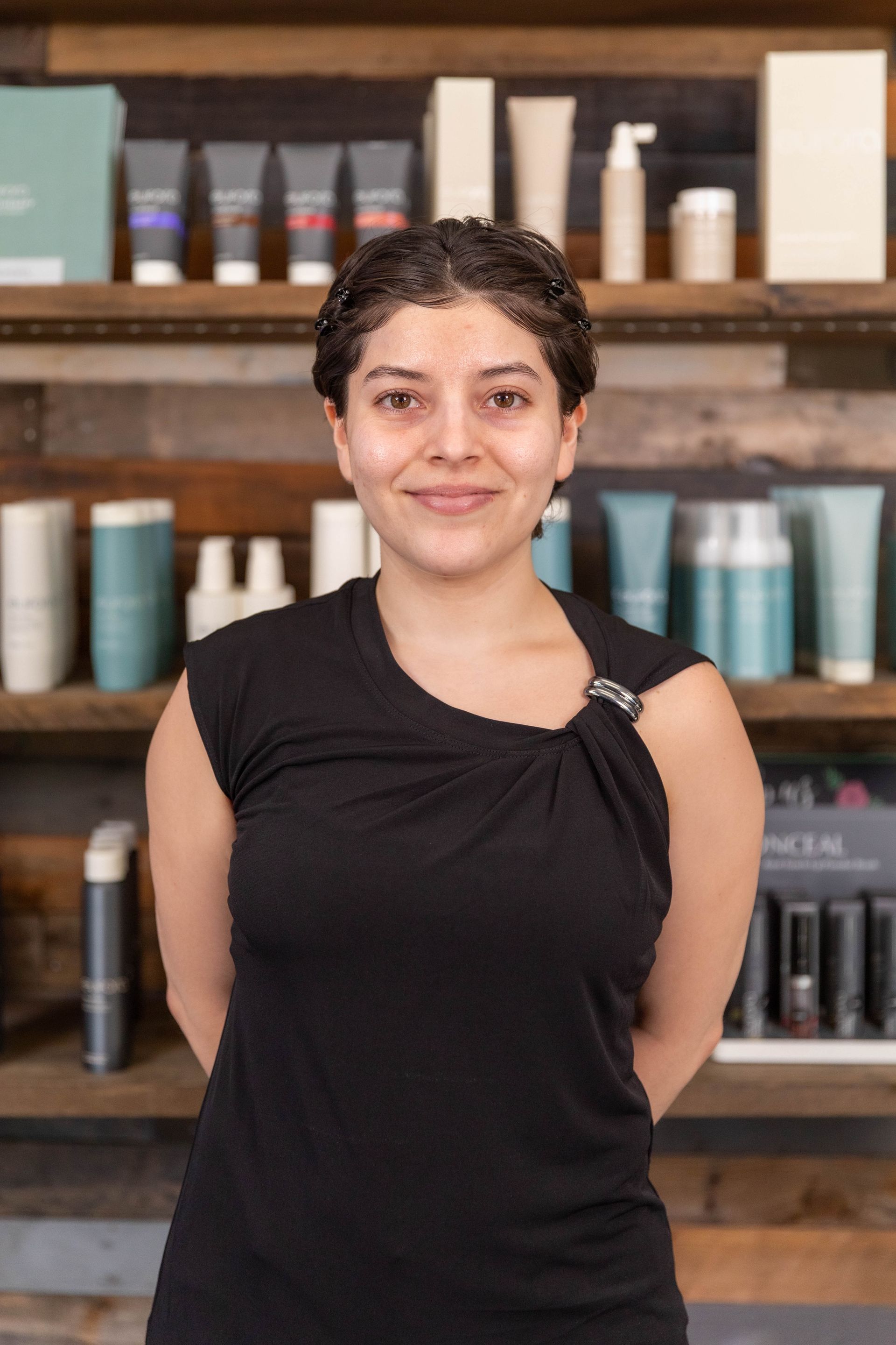 Person smiling in a black top, standing in front of shelves with hair products.
