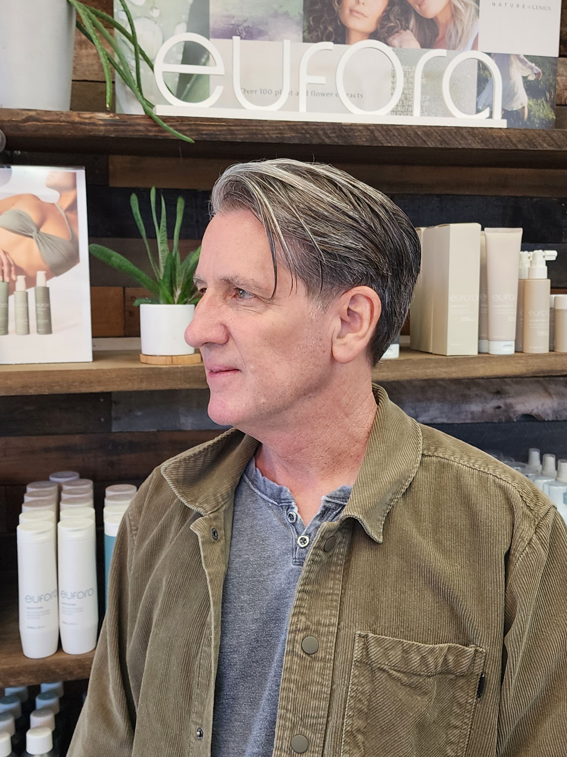 Man with gray hair, wearing a green corduroy jacket, stands in a salon.