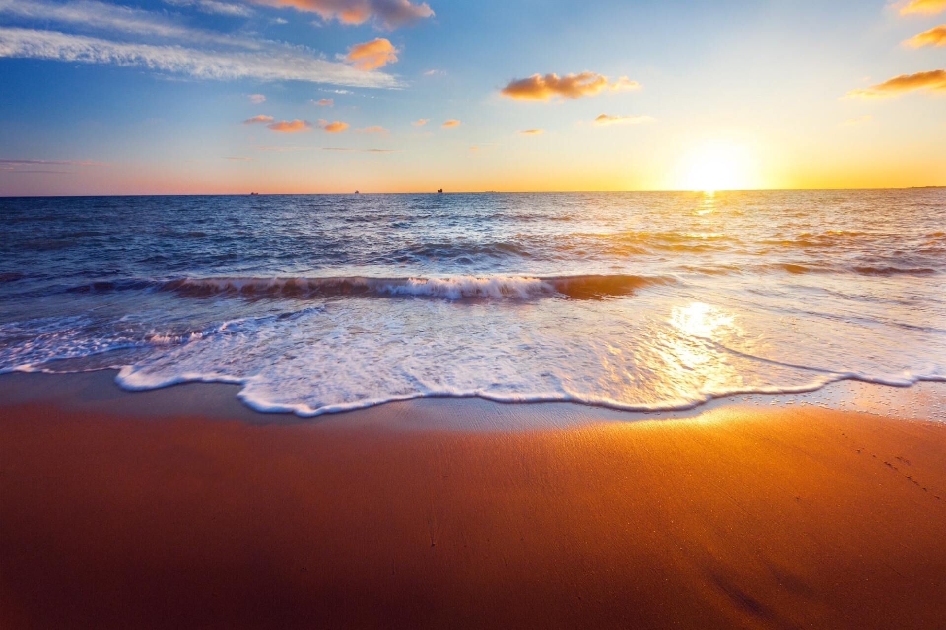 The sun is setting over the ocean and the waves are crashing on the beach.