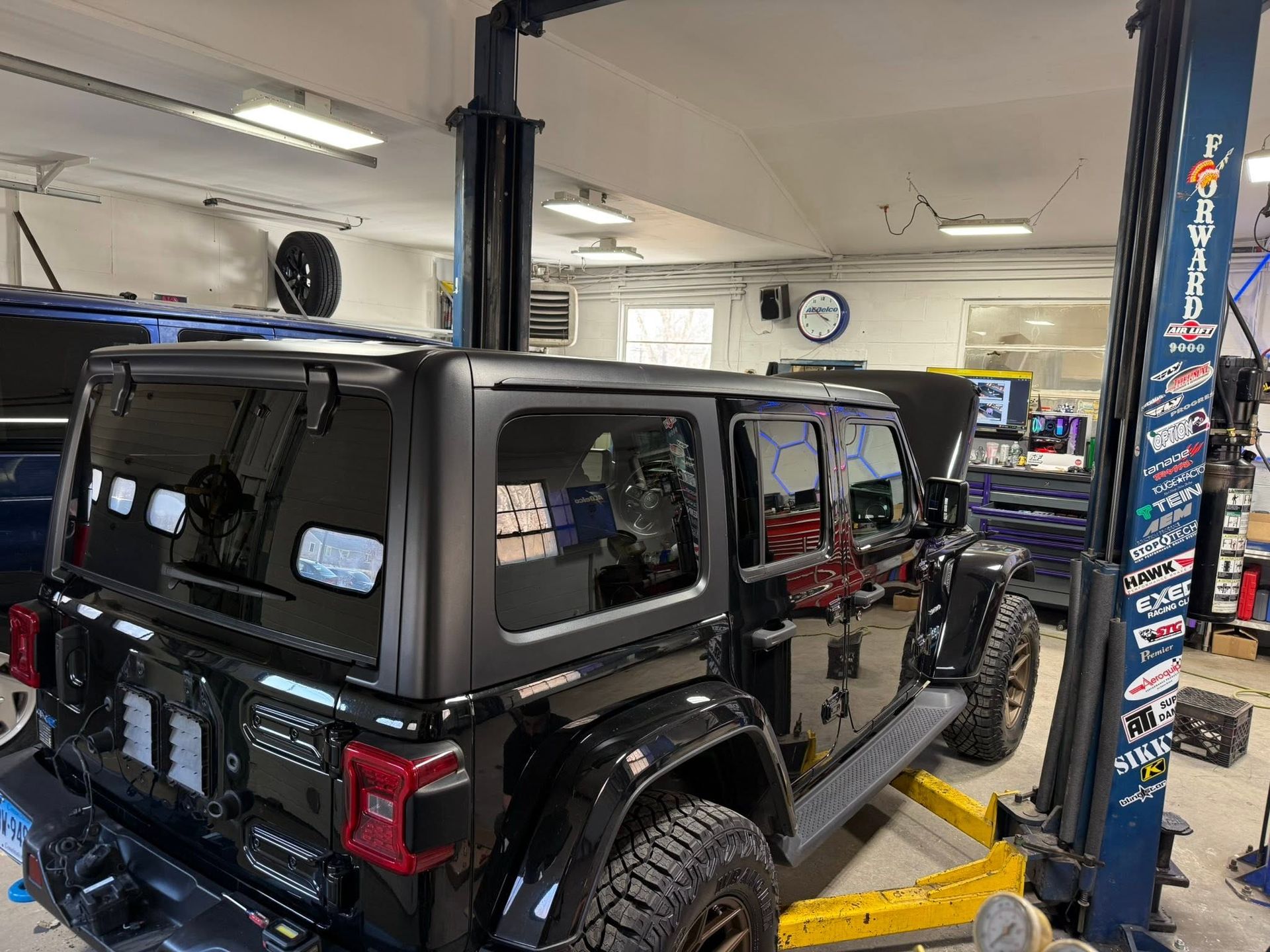 Black Jeep Wrangler in a garage on a lift beside a workbench and tools