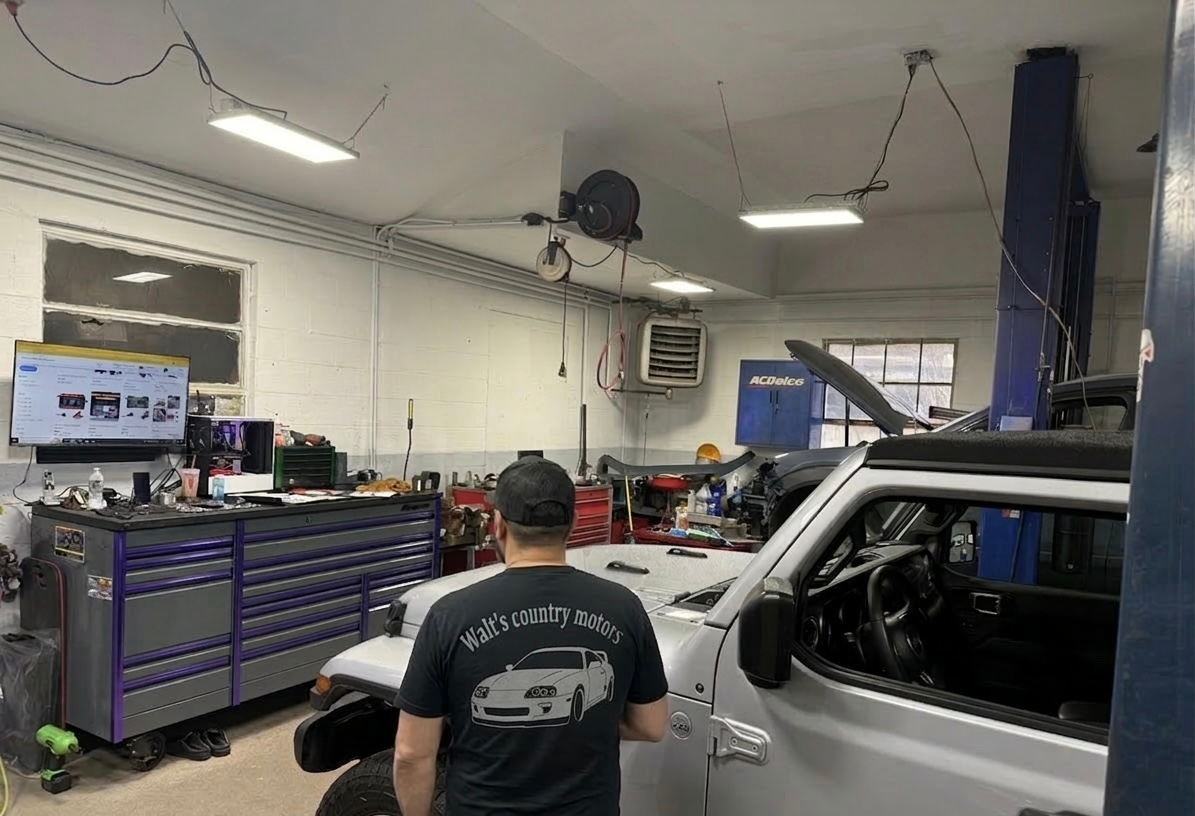 Auto shop interior with a mechanic working beside a white truck and tool benches.