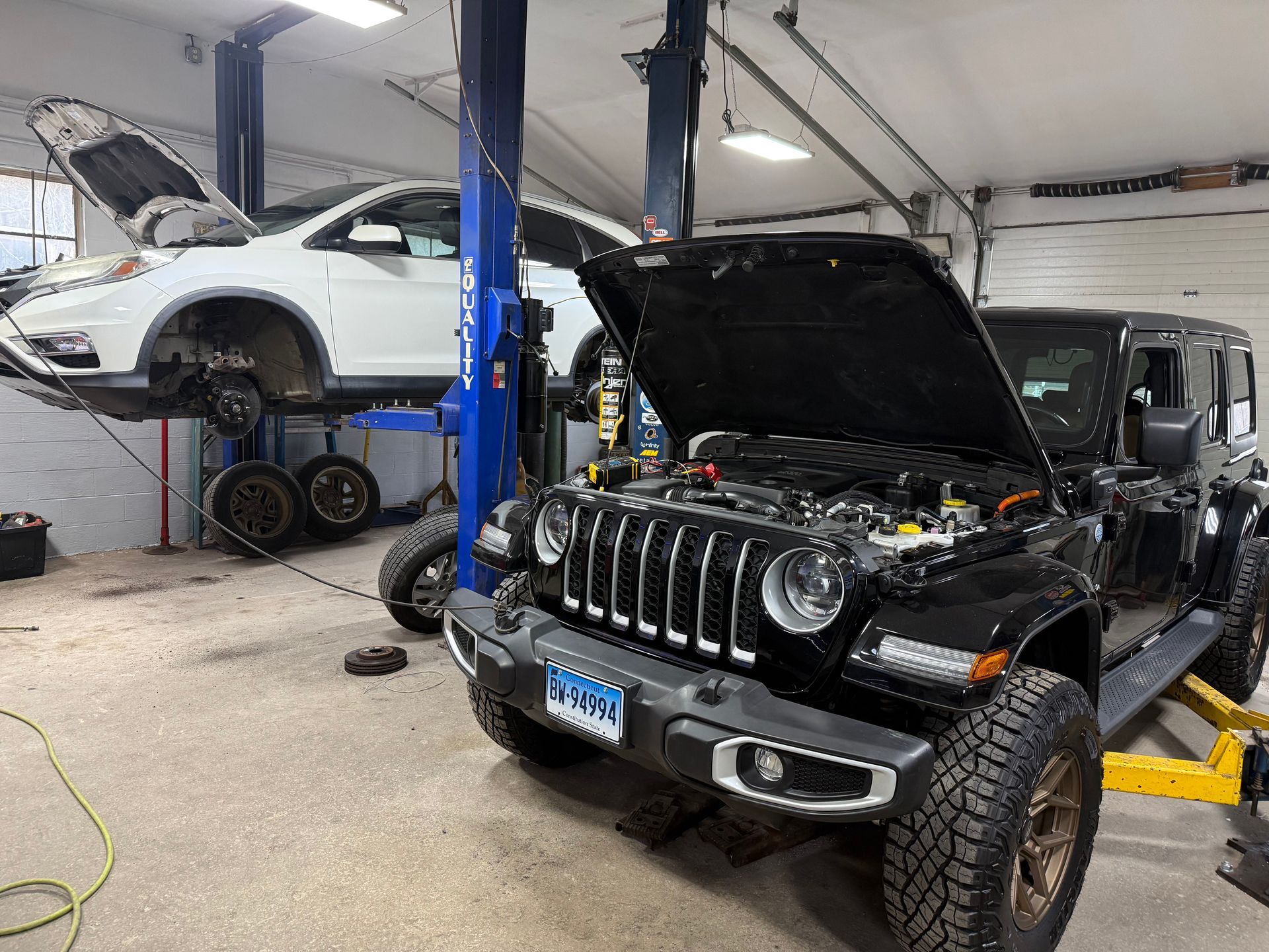 Auto repair shop with a black Jeep and white SUV on lifts, both with open hoods.