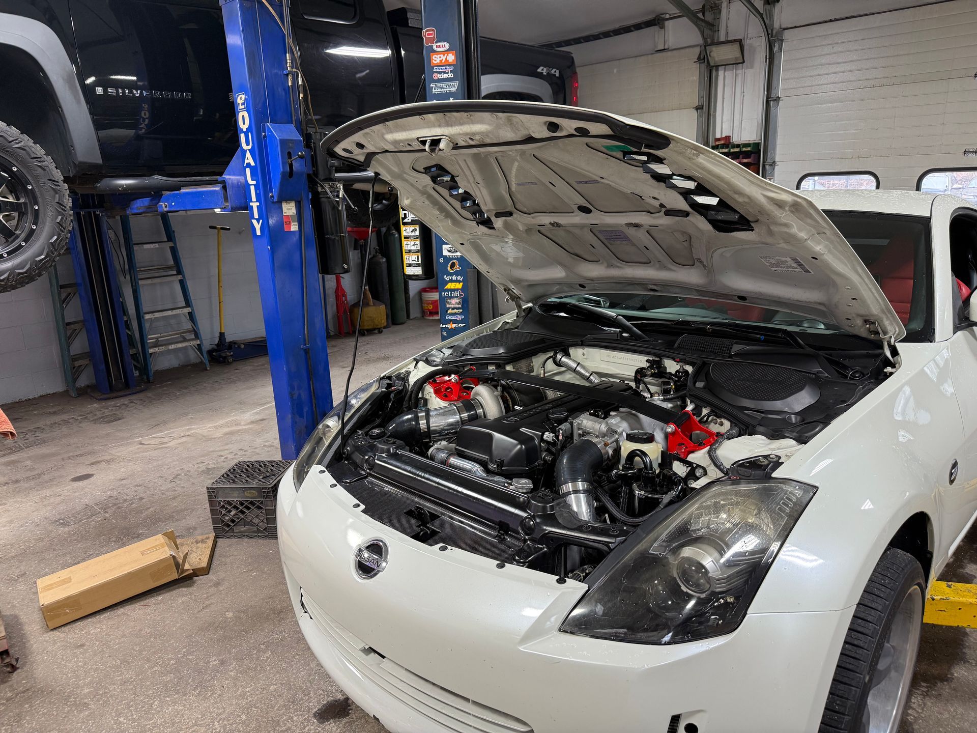 White sports car with hood open in a garage, showing its engine bay on a lift