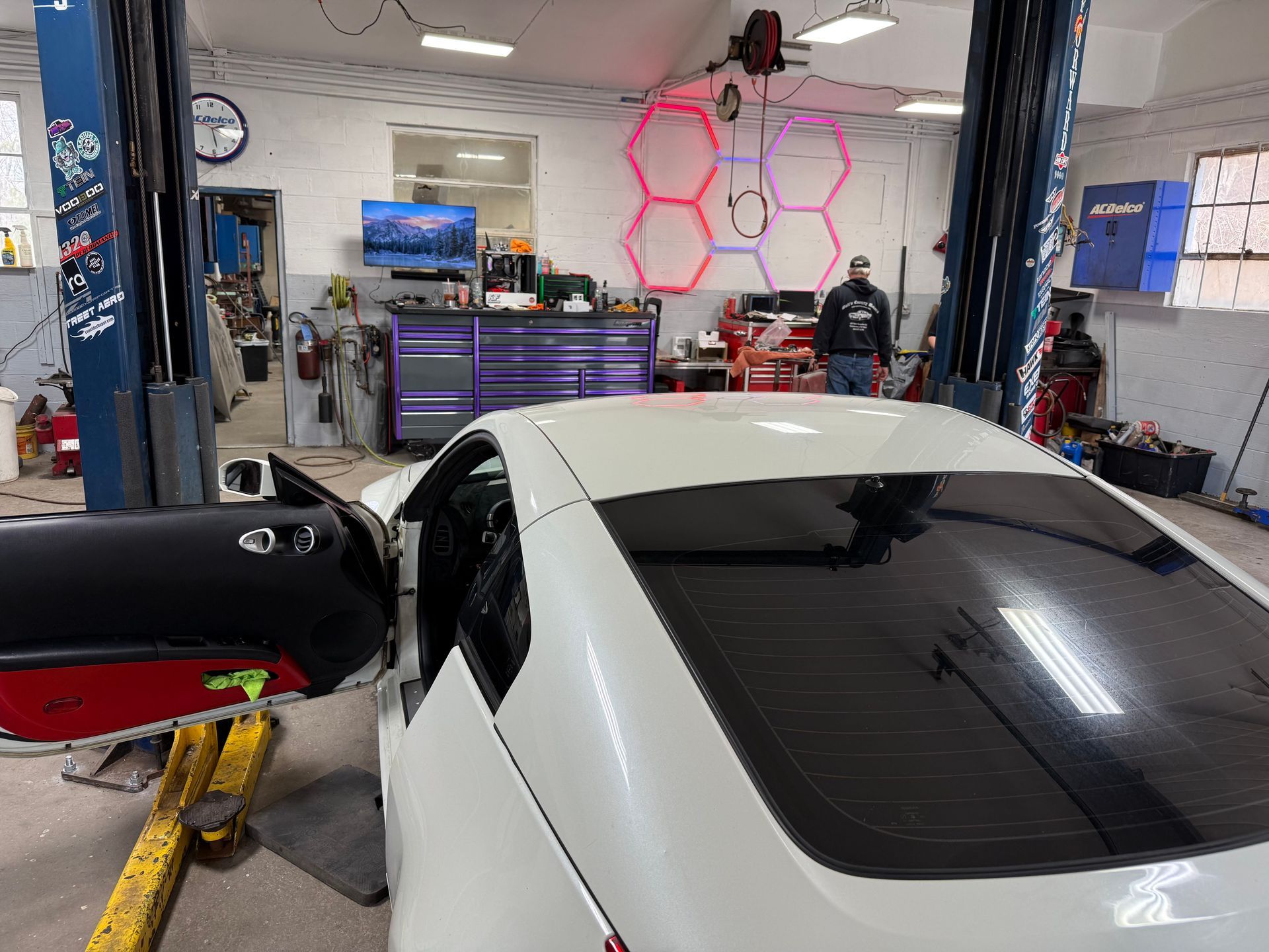 White car in an auto shop with its door open, parked on a lift inside a garage.