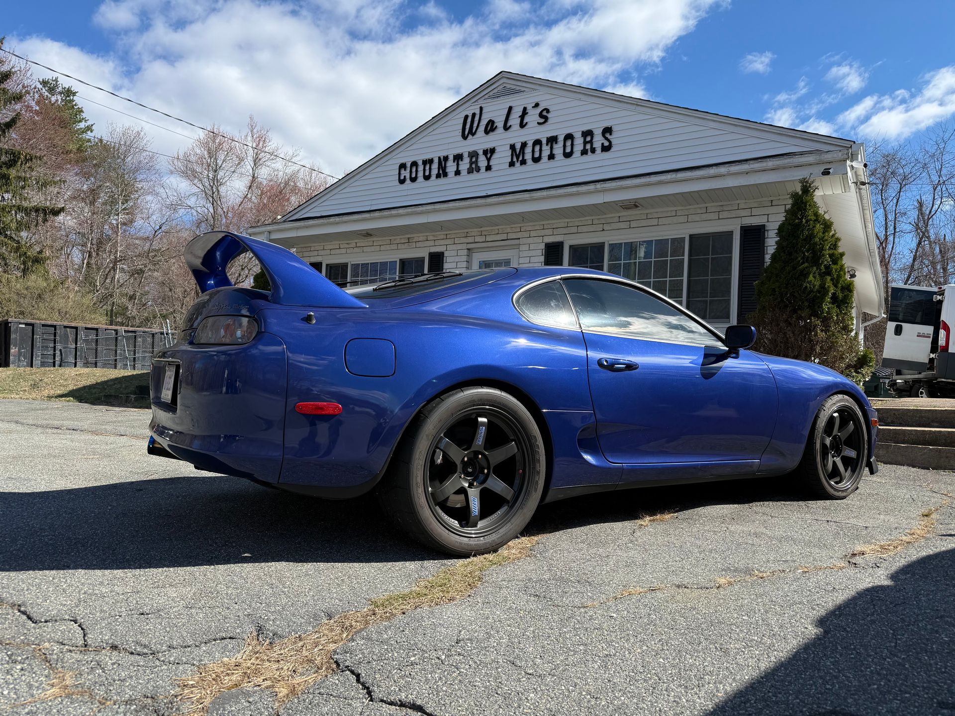 Blue sports coupe parked outside a stone building labeled “B.J.’s Country Motors”